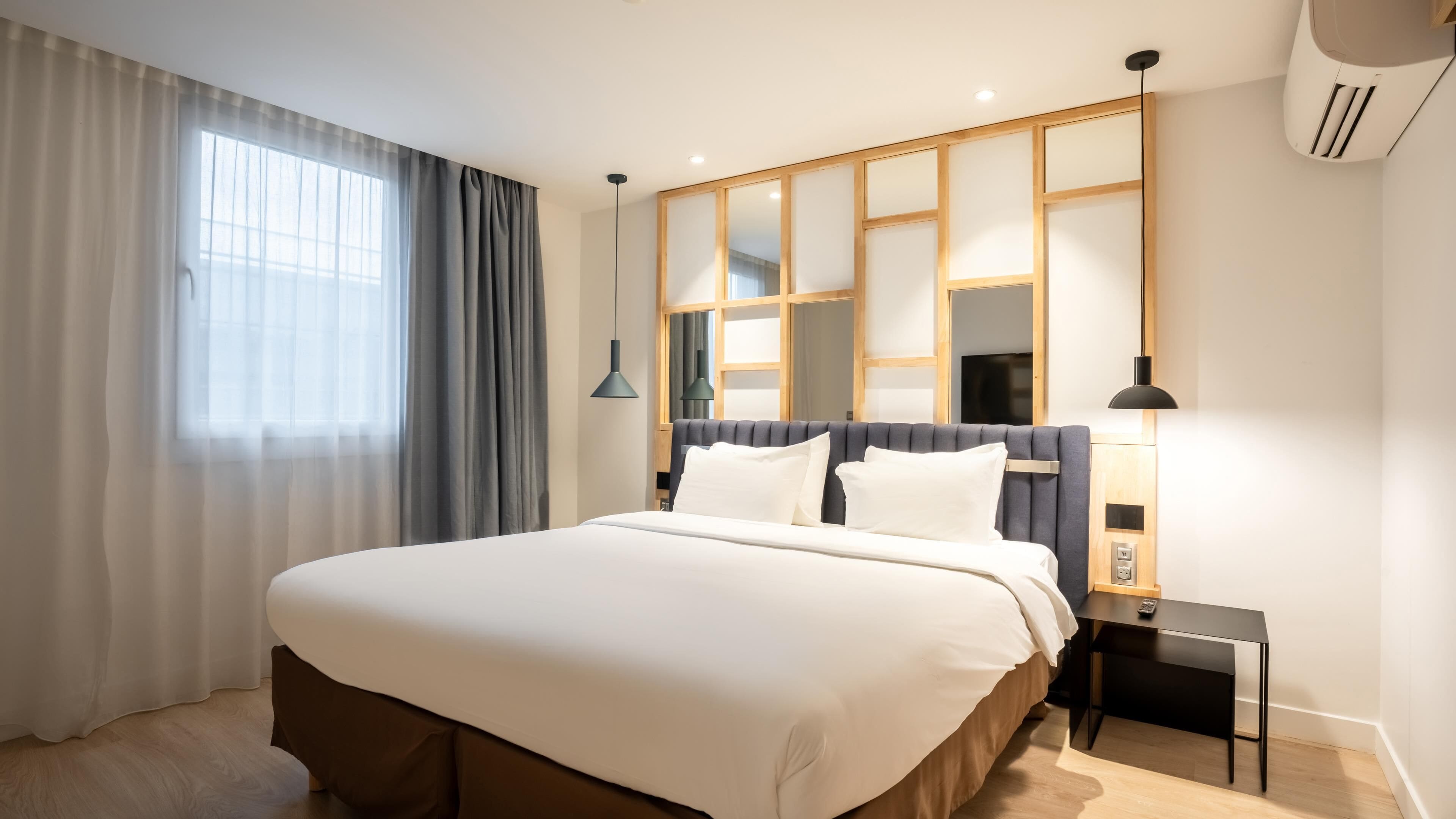 Ein modernes Hotelzimmer mit einem großen Bett, einem Nachttisch, einer Lampe und einem Fenster mit Vorhängen.