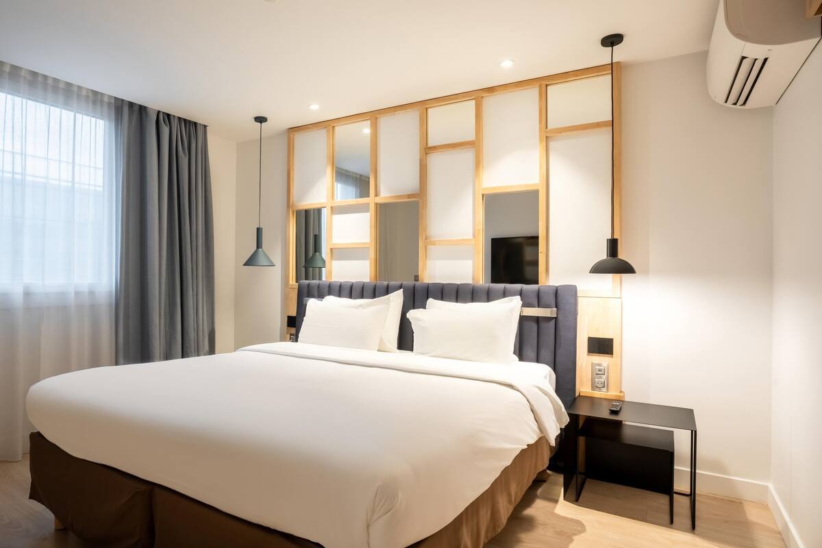 A modern hotel room with a large bed, a nightstand, a lamp, and a window with curtains.