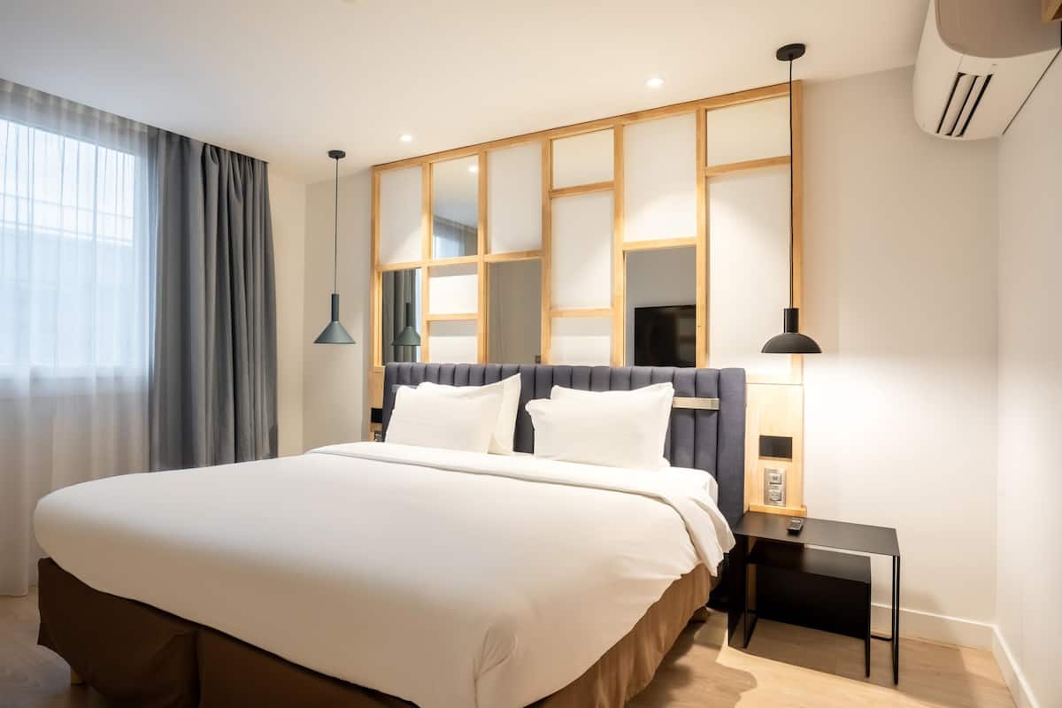 A modern hotel room with a large bed, a nightstand, a lamp, and a window with curtains.