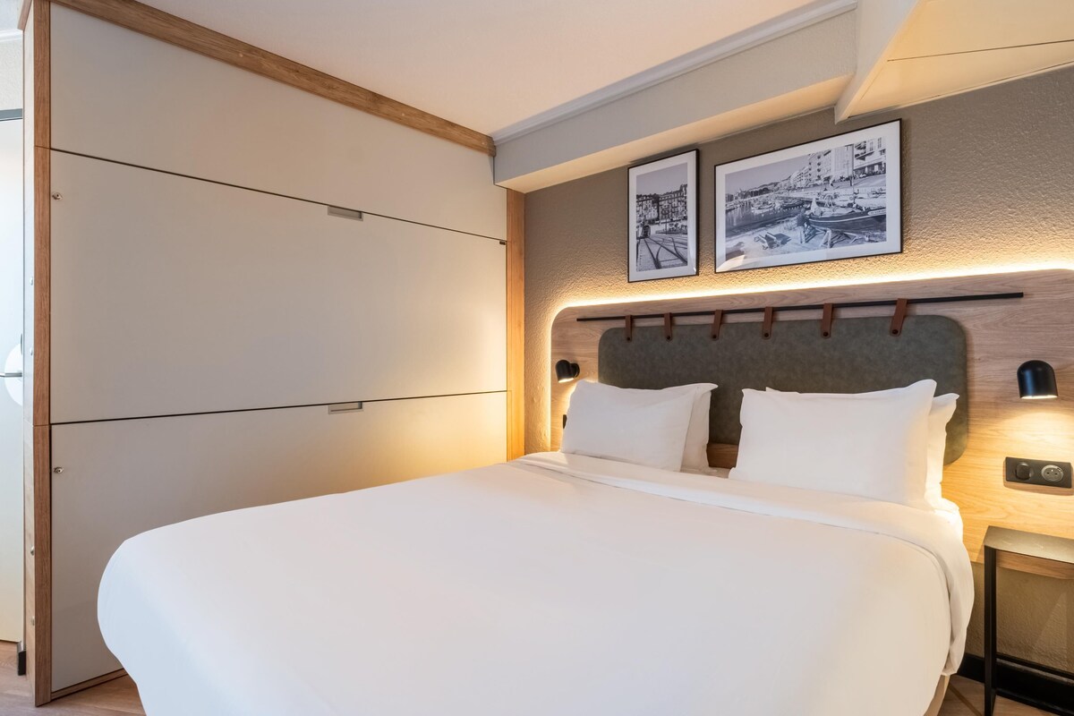 A neatly made bed with a headboard, bedside lamps, and two framed pictures on the wall.