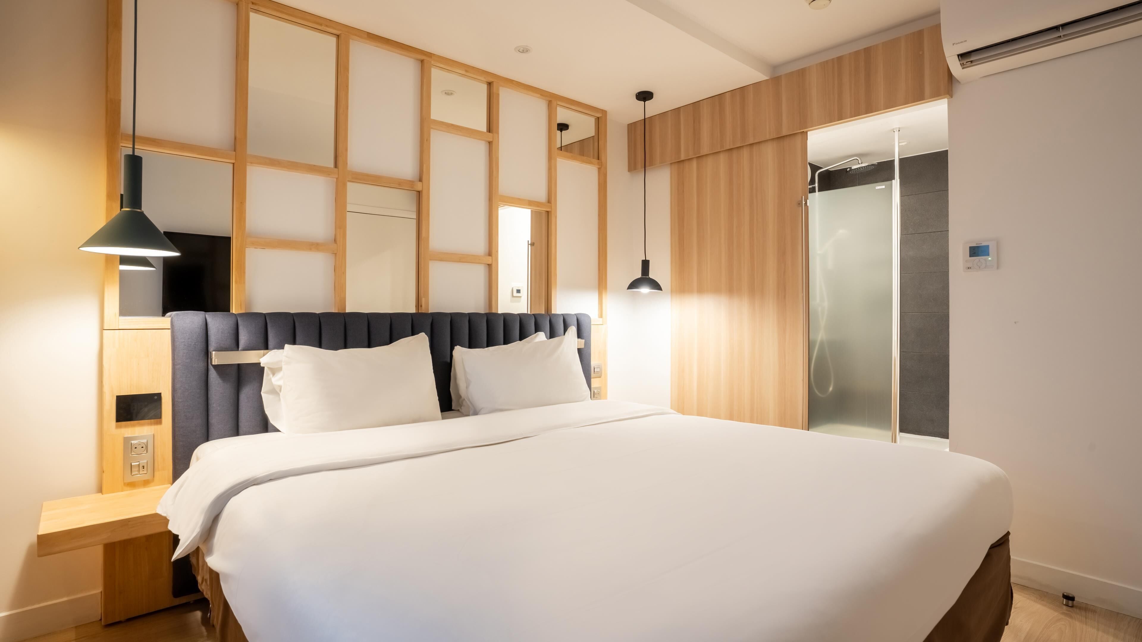 Une chambre d’hôtel moderne dotée d’un grand lit, de tables de chevet, d’une armoire et d’un espace douche.