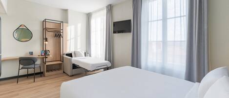 A hotel room with a bed, a desk, a chair, a TV, and large windows with curtains.