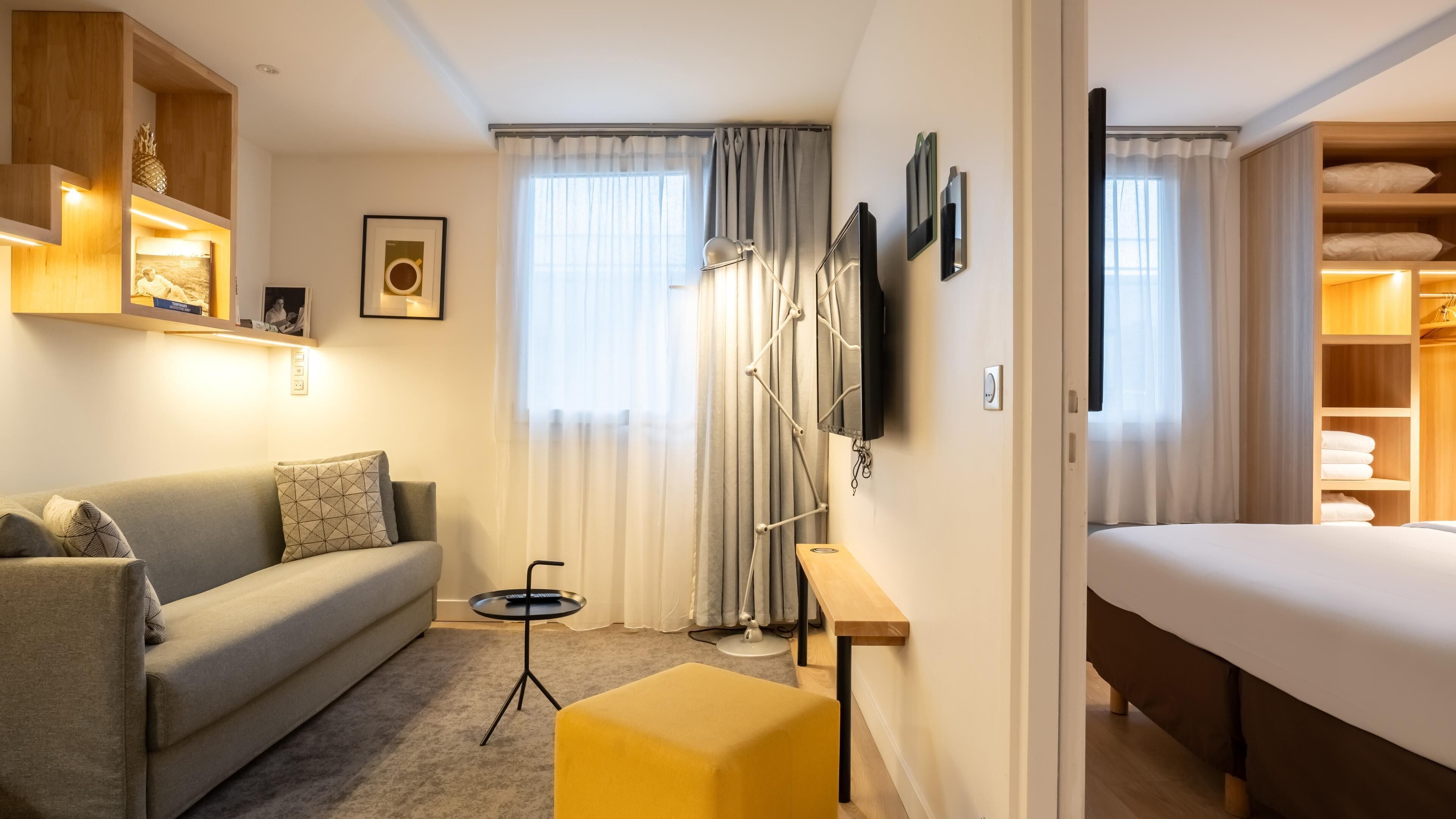 A hotel room with a sofa, a small table, a bed, a TV, and a wardrobe.