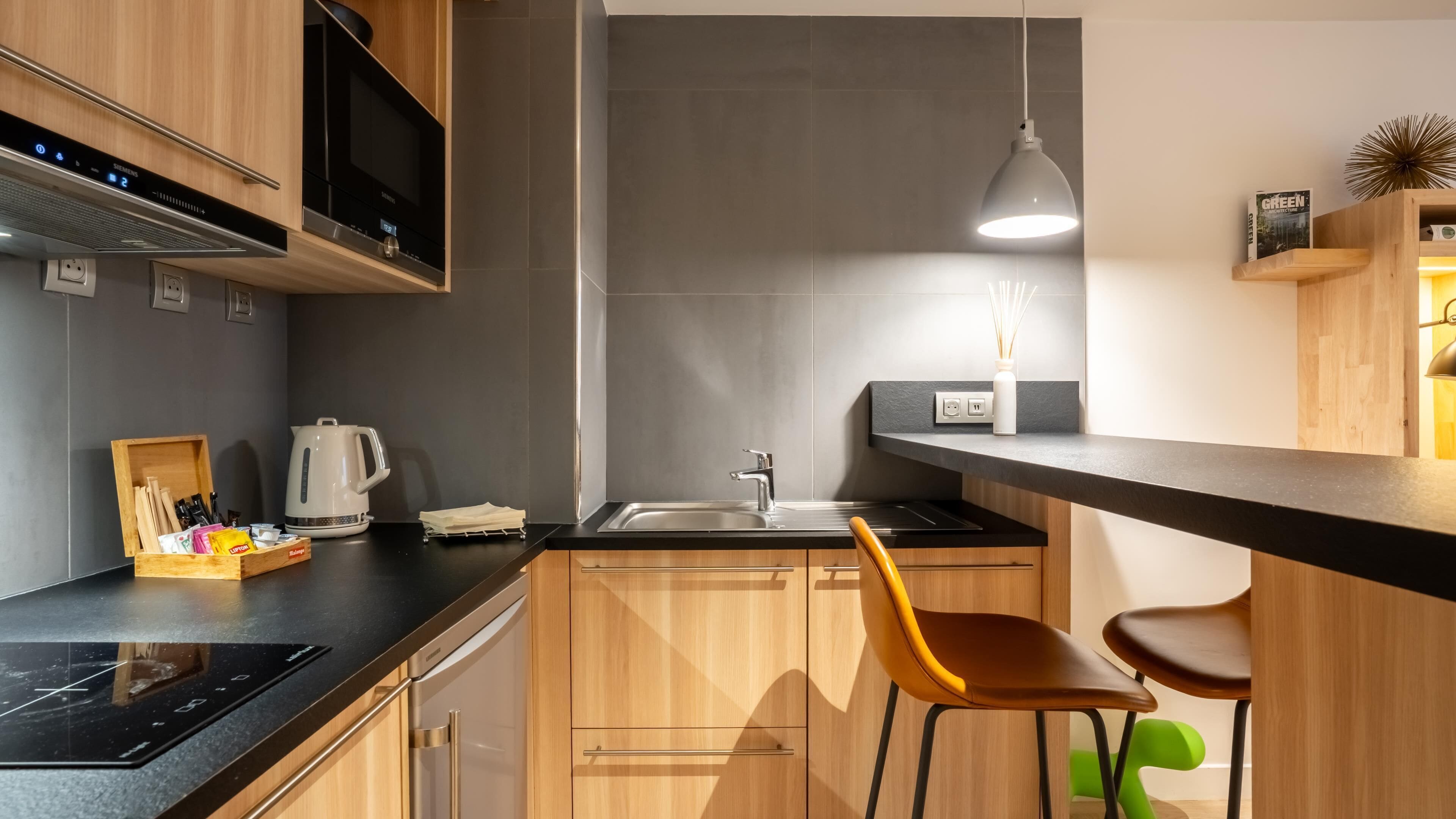 A modern kitchen with a built-in microwave, a kettle, a sink, and a bar area with stools.