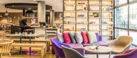 A modern lounge area with a purple sofa, round tables, and a bookshelf filled with books.
