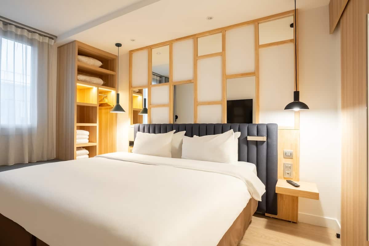 A hotel room with a large bed, wooden wardrobe, and a bedside table with a lamp.