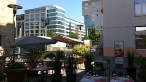 An outdoor café with tables and chairs, surrounded by potted plants and umbrellas. - Campanile PRIME - Saint-Quentin-en-Yvelines (Montigny-le-Bretonneux)
