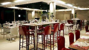 A spacious dining area with multiple tables and chairs, featuring a modern design with a mix of red and white chairs. - Campanile PRIME - Saint-Quentin-en-Yvelines (Montigny-le-Bretonneux)