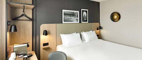 Habitación de hotel con cama, mesita de noche, silla, escritorio, televisión y lámparas de pared.