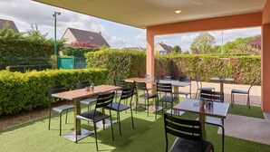 An outdoor patio area with tables and chairs, surrounded by greenery and a view of the neighborhood. - Campanile NATURE - Meaux (Meaux)