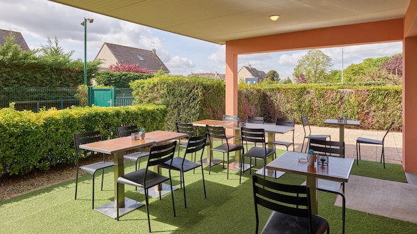 An outdoor patio area with tables and chairs, surrounded by greenery and a view of the neighborhood. - Campanile NATURE - Meaux (Meaux)
