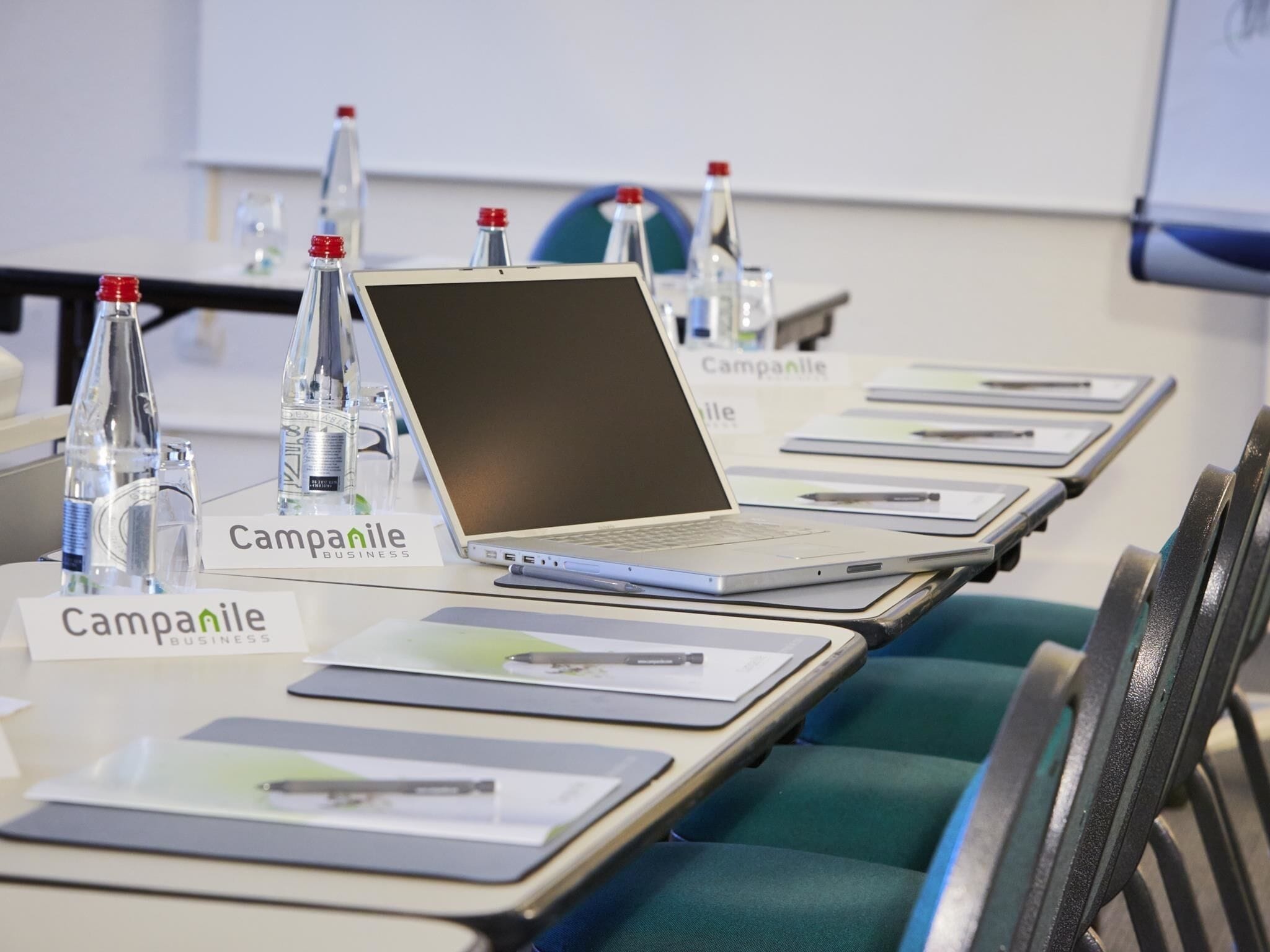 Une salle de conférence équipée de tables, d’ordinateurs portables, de plaques nominatives et de bouteilles d’eau.