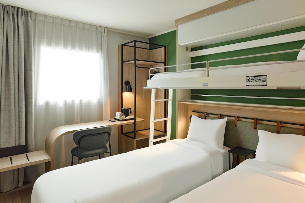 A hotel room with two beds, a desk, a chair, a ladder, and a window with curtains.
