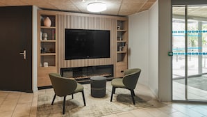 Ett modernt vardagsrum med en platt-TV, en öppen spis och två gröna fåtöljer.