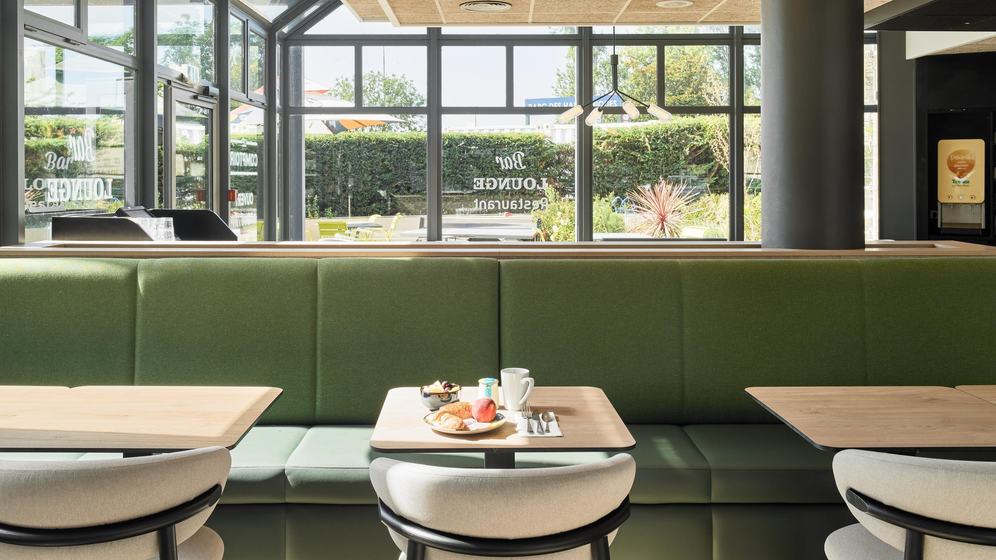 Un restaurante con zona de estar con bancos acolchados de color verde, mesas y vistas amplias a través de grandes ventanales.