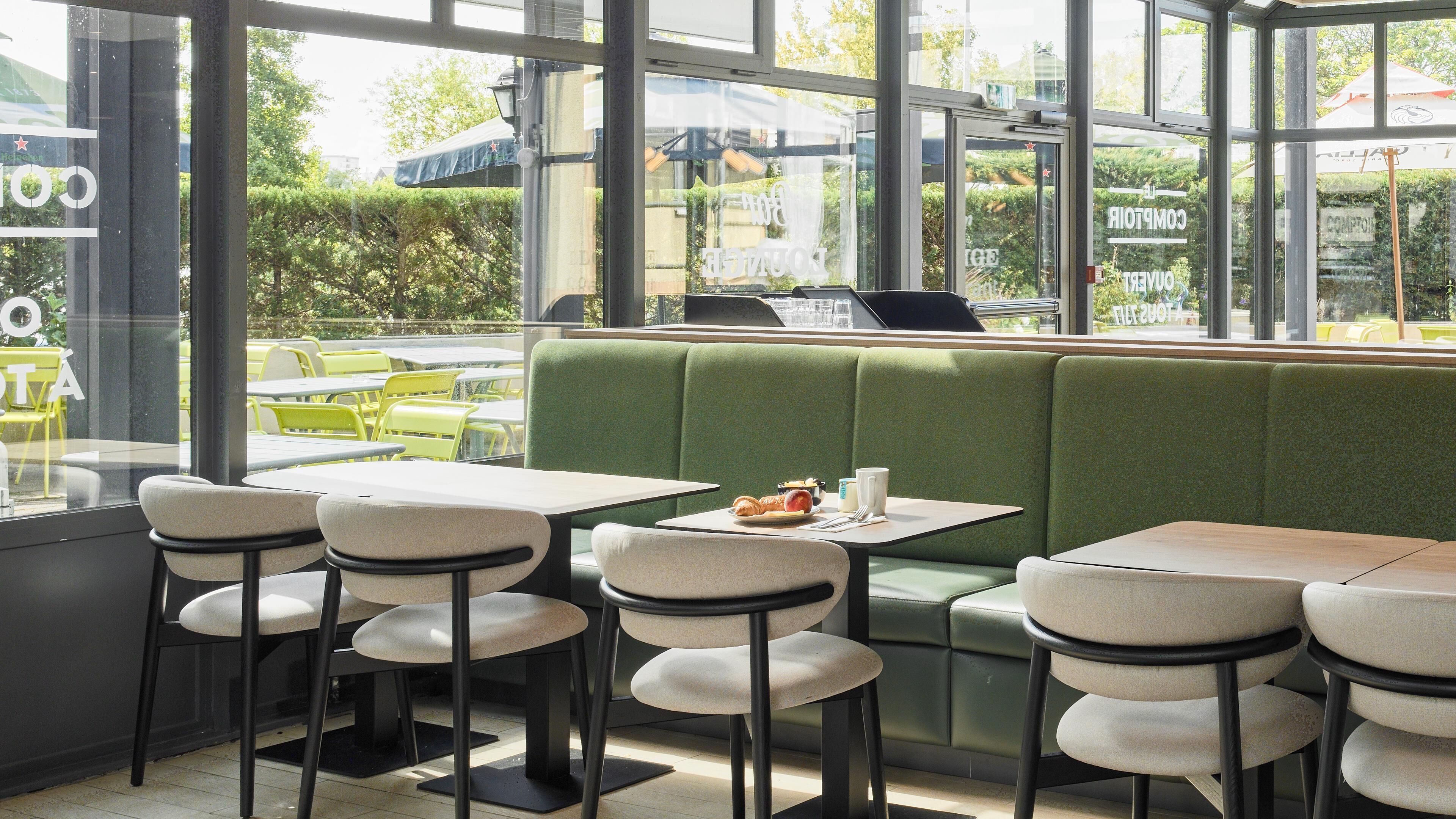 Un restaurante con asientos de tapicería verde, mesas y sillas blancas.
