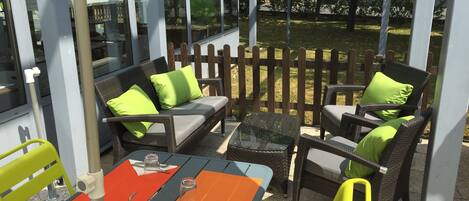 An outdoor patio with wicker furniture, a glass table, and a wooden fence.