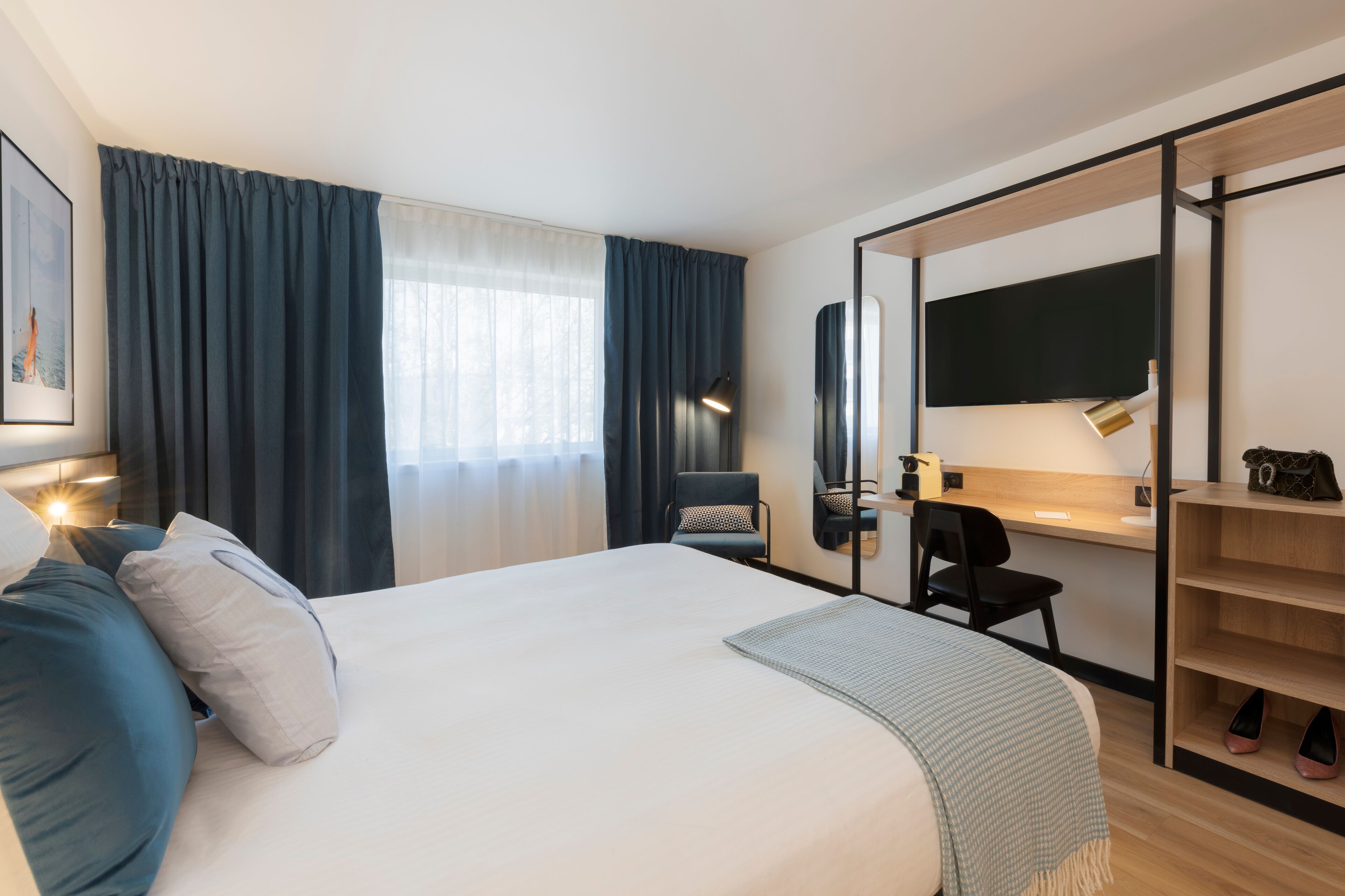 A hotel room with a large bed, a desk with a chair, a TV, and a wardrobe.