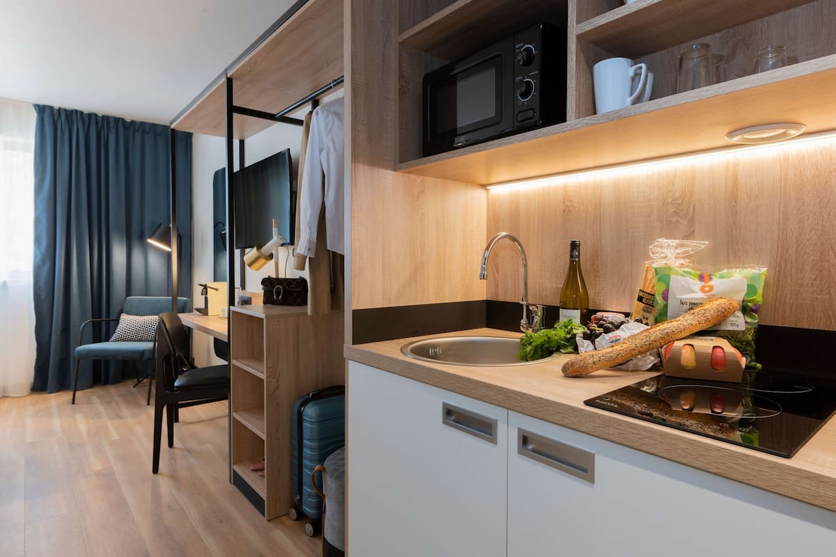 A compact kitchenette with a microwave, sink, and a bottle of wine.