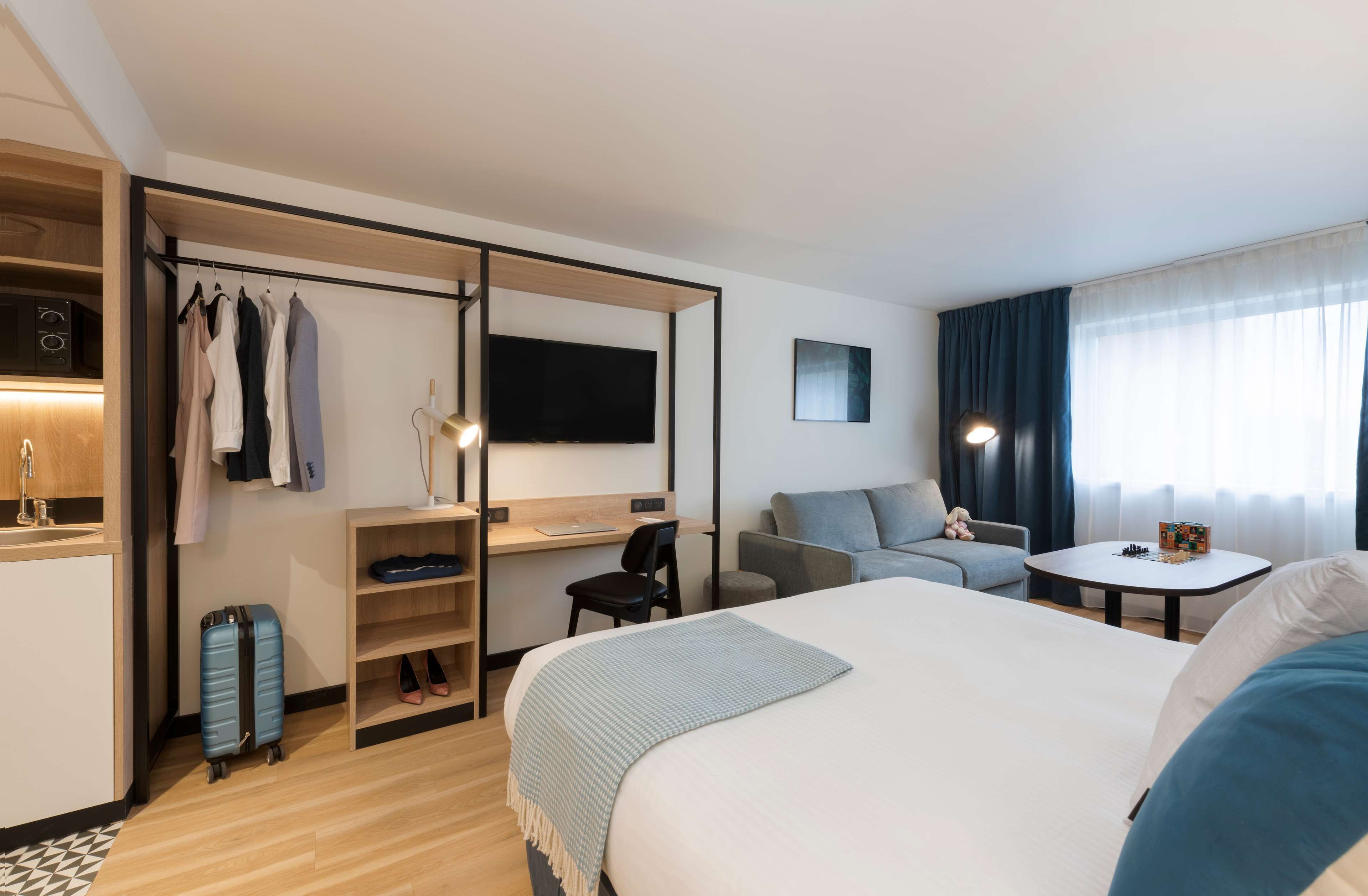 Habitación de hotel con cama, escritorio, silla, televisor, mesita y ventana con cortinas.