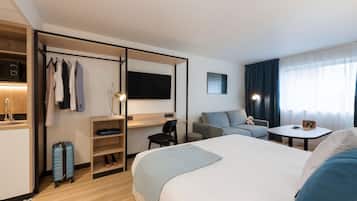 A hotel room with a bed, a desk, a chair, a TV, a small table, and a window with curtains.