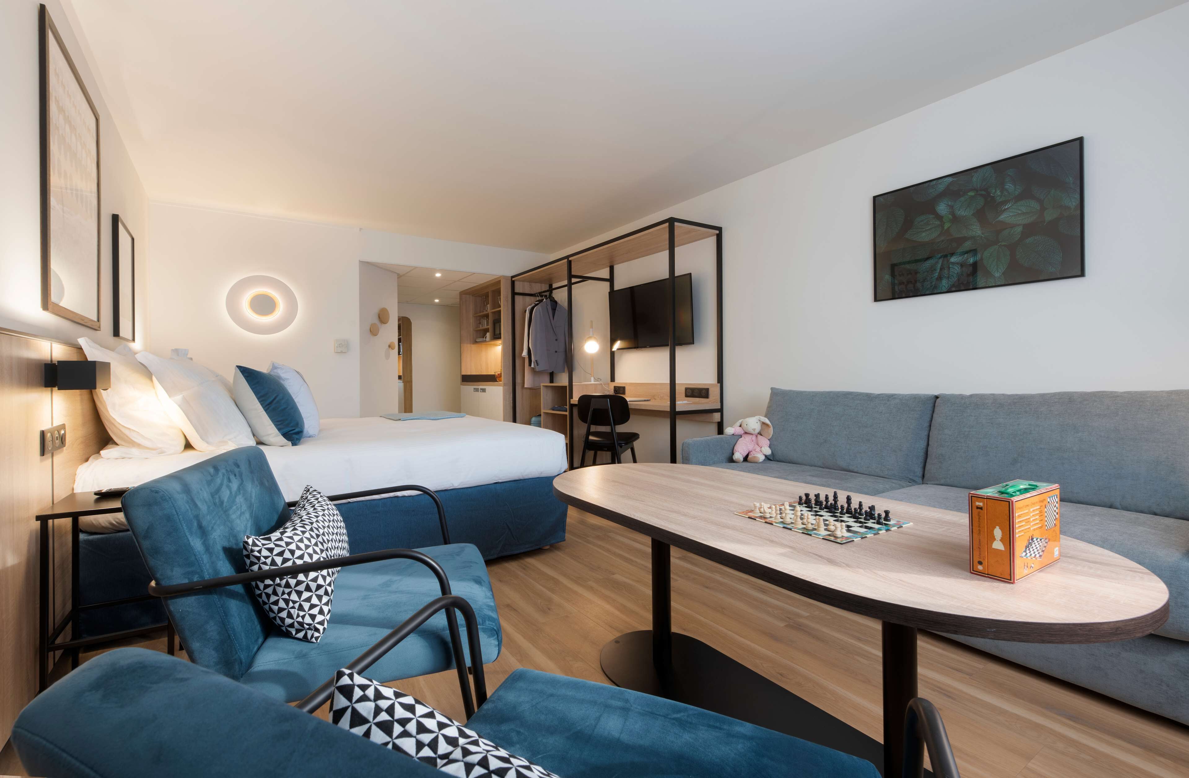 Ein modernes Hotelzimmer mit Bett, Sofa und Esstisch mit Schachspiel.