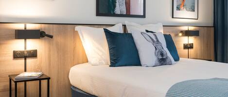 A modern hotel room with a large bed, wooden headboard, and two bedside tables with lamps.