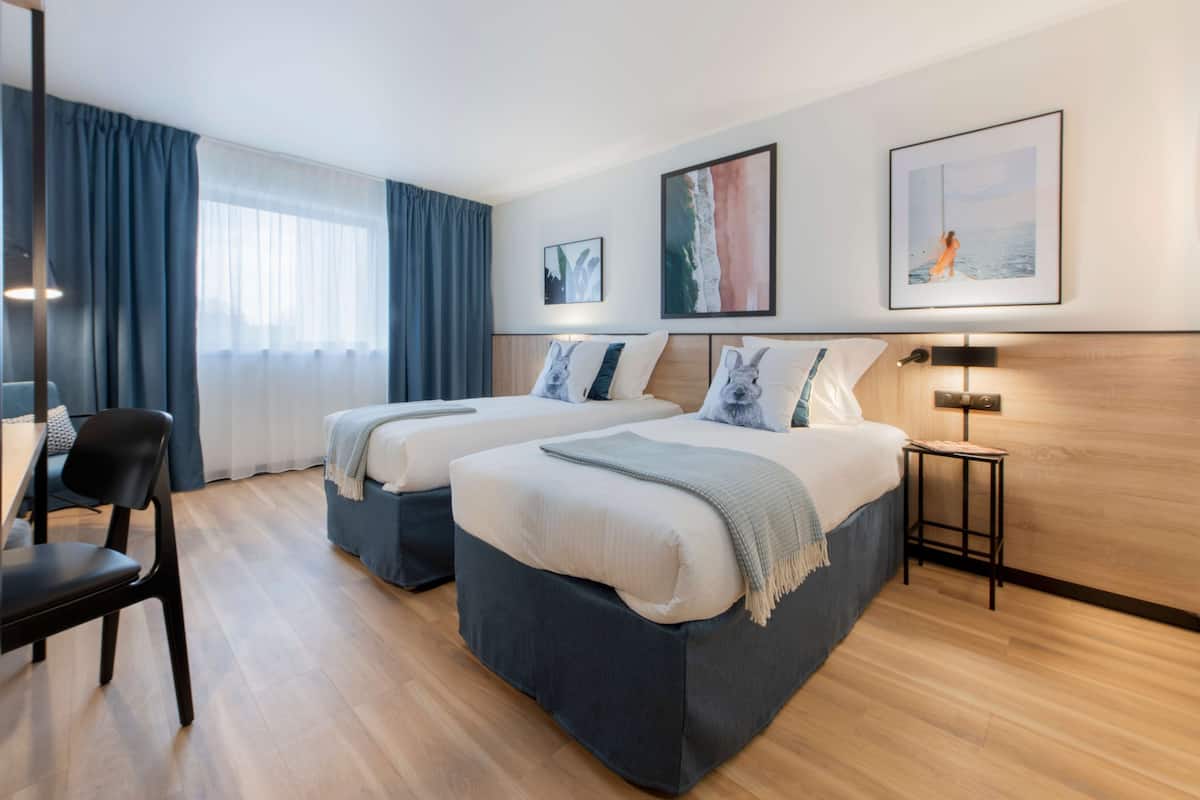 A hotel room with two beds, a desk, and a chair.
