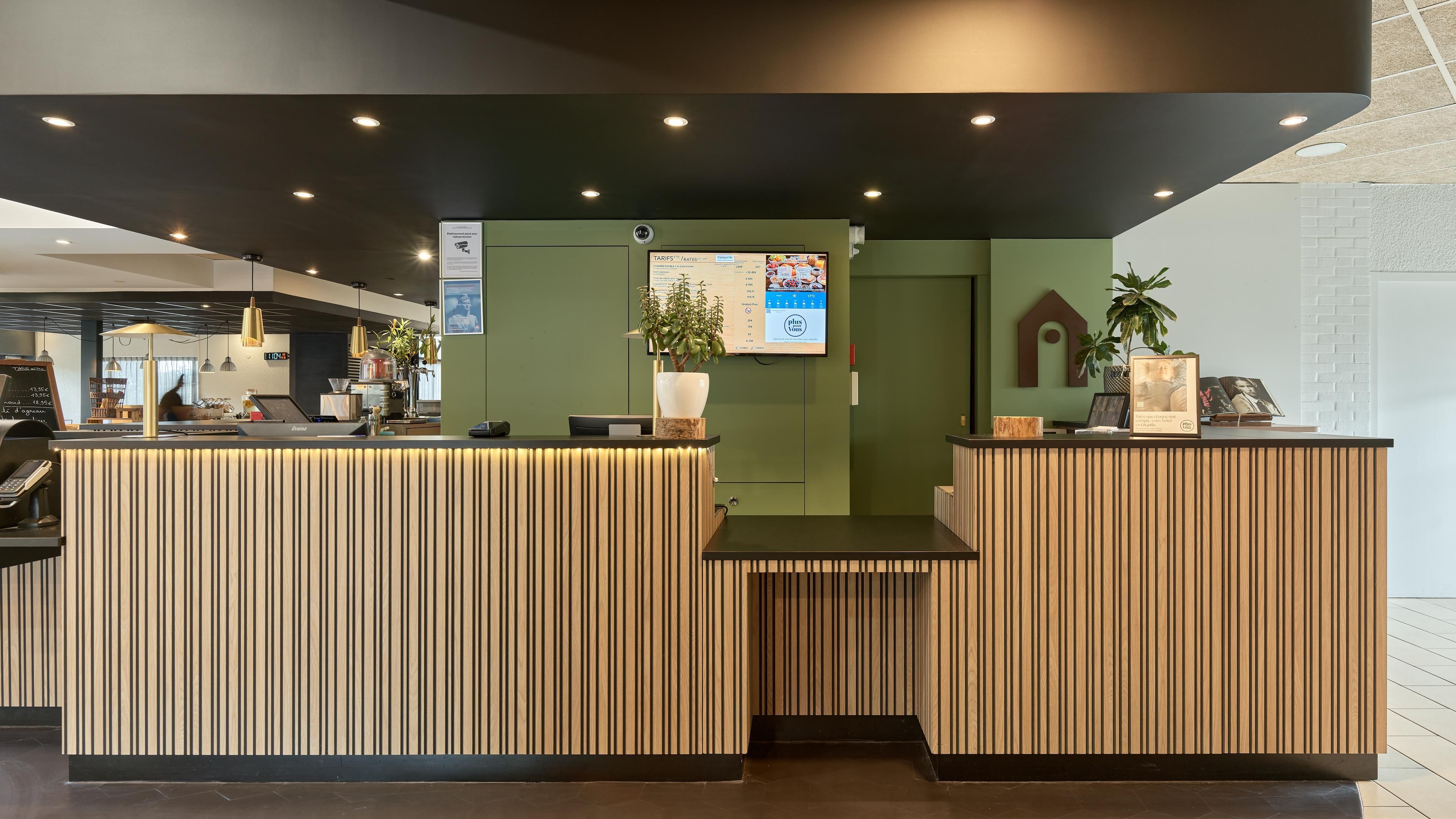 Una zona reception con una scrivania in legno, uno schermo digitale che mostra le tariffe e una parete verde.