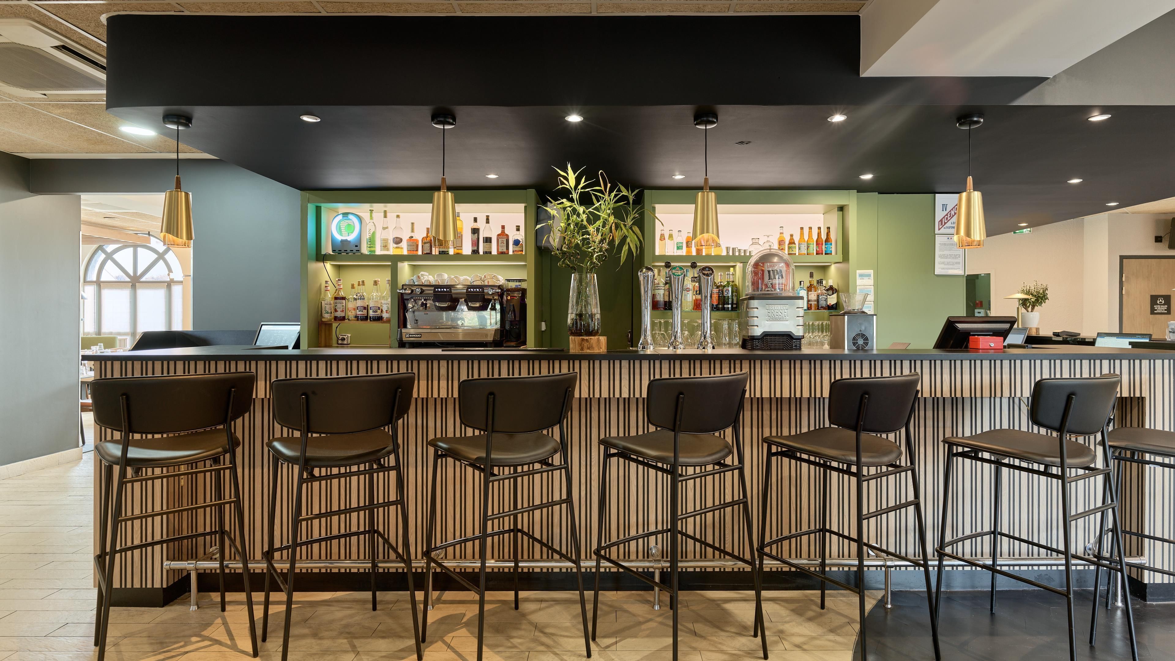 Un espace bar comprenant un comptoir, des tabourets de bar et une variété de bouteilles et de verres.