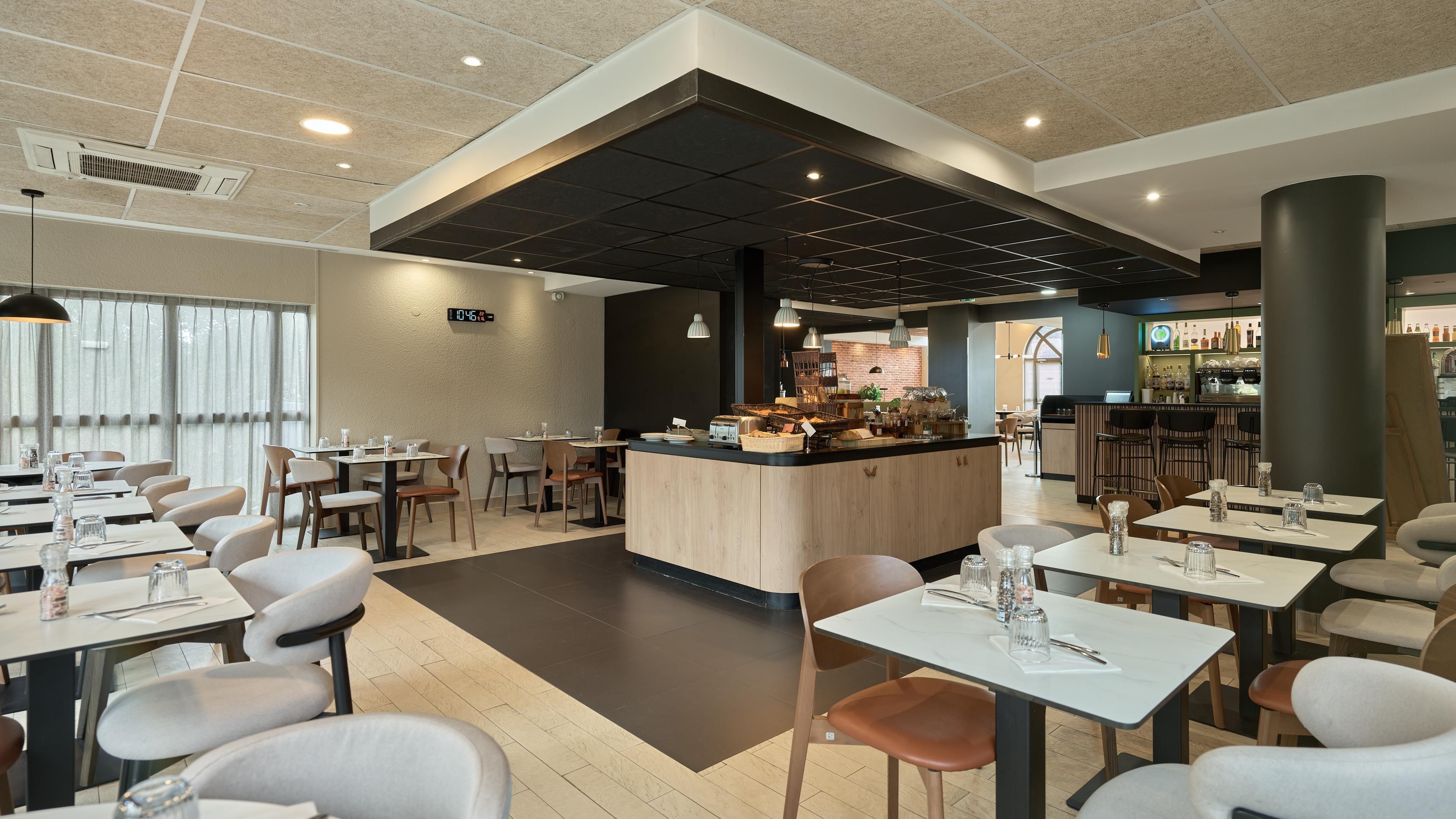 A modern cafe with a central bar area, multiple seating options, and a digital clock on the wall.