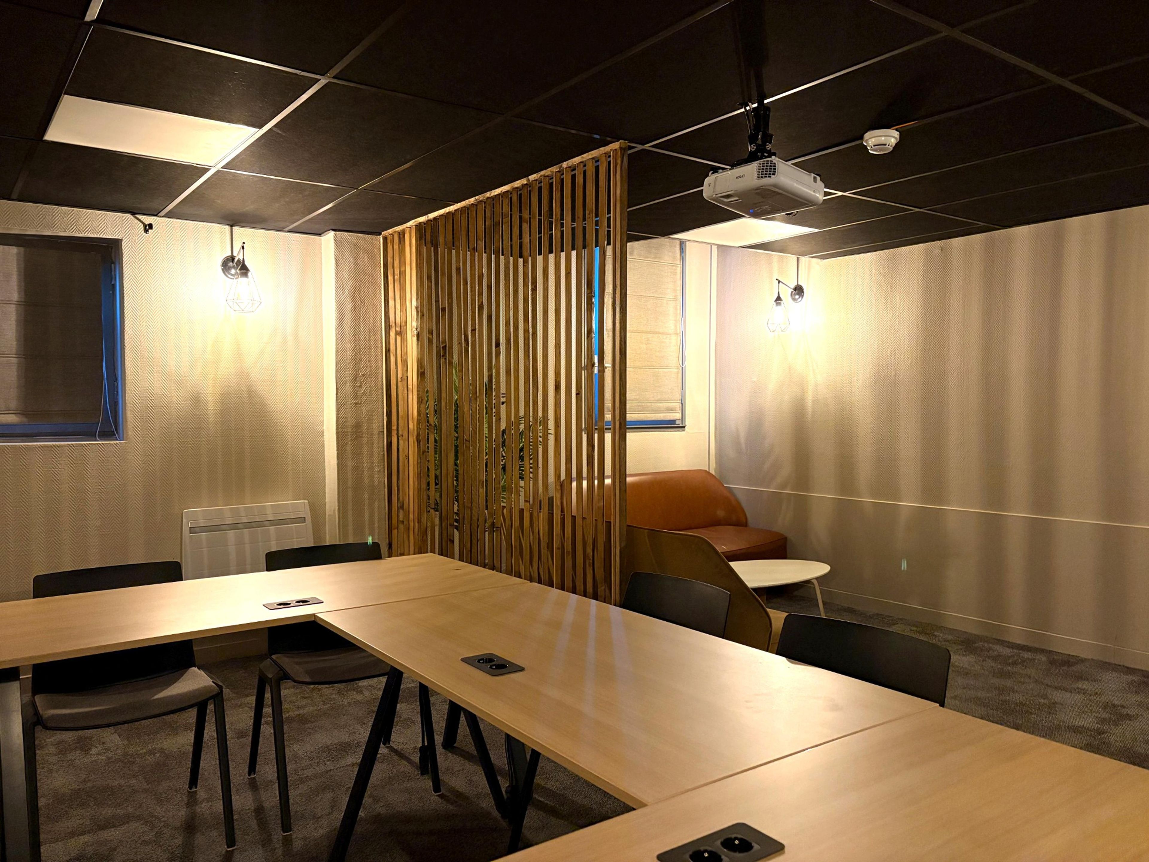 Een vergaderzaal met een lange tafel, stoelen, een beamer en een scheidingswand.