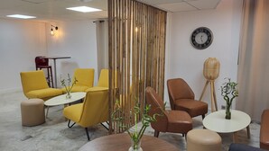 A modern conference room with yellow and brown chairs, a wooden divider, a round wooden table, a clock on the wall, and a projector on the ceiling. - Campanile PRIME - Villejuif (Villejuif)