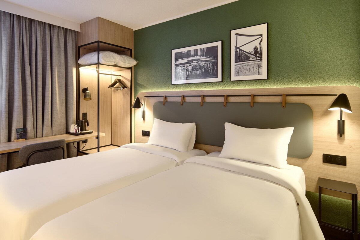 A hotel room with a bed, desk, and two framed pictures on the wall.