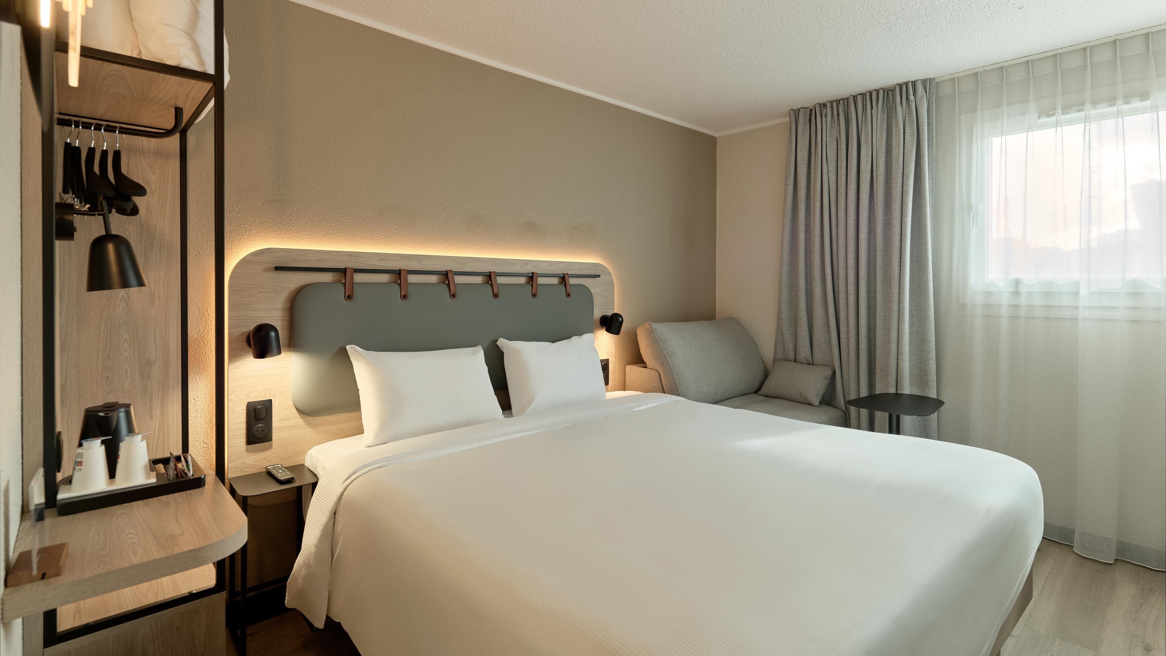 Une chambre d’hôtel avec un grand lit, des tables de chevet, une lampe, un canapé et une fenêtre avec des rideaux.