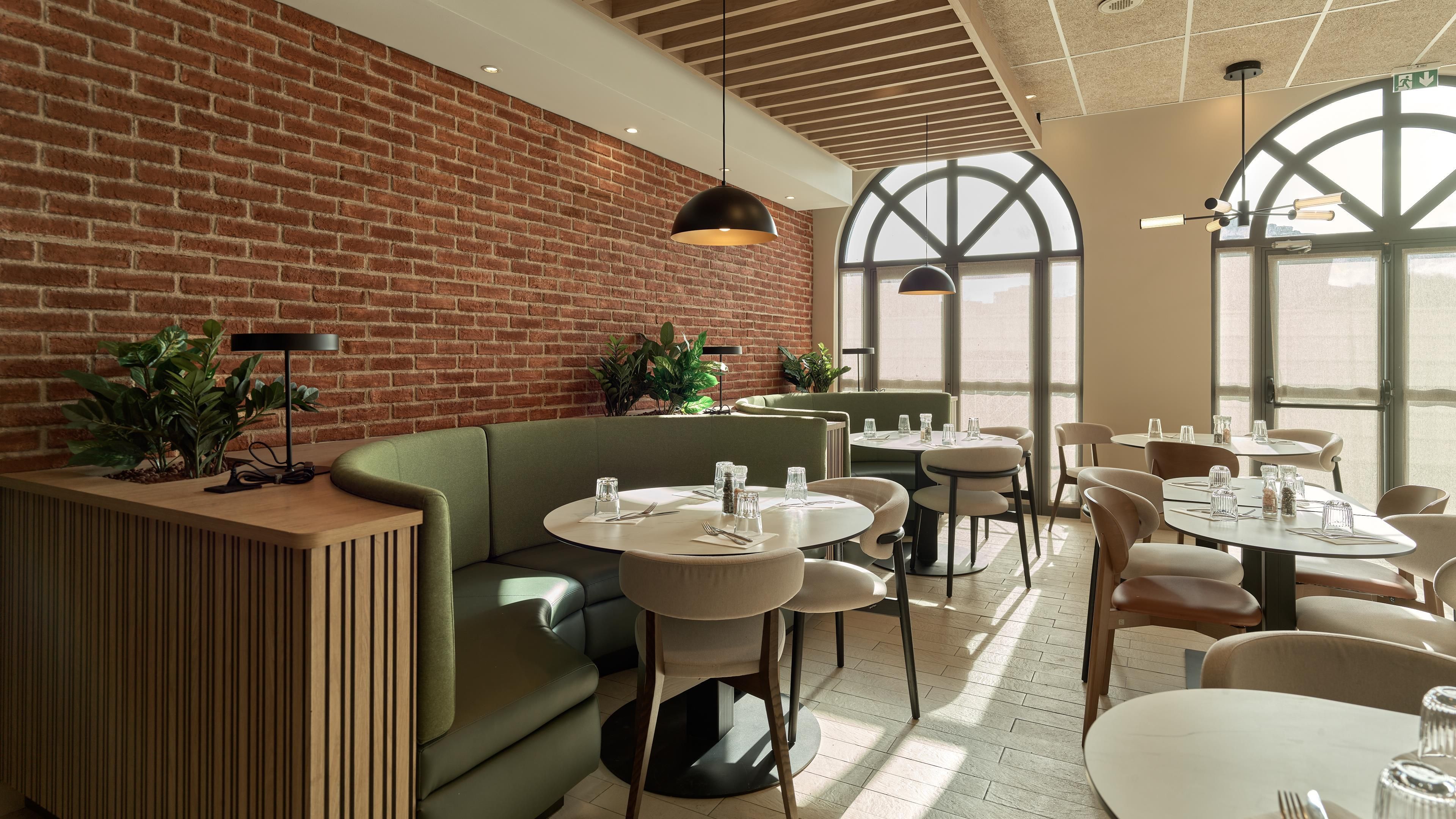 A restaurant interior with brick walls, round tables, and green seating.