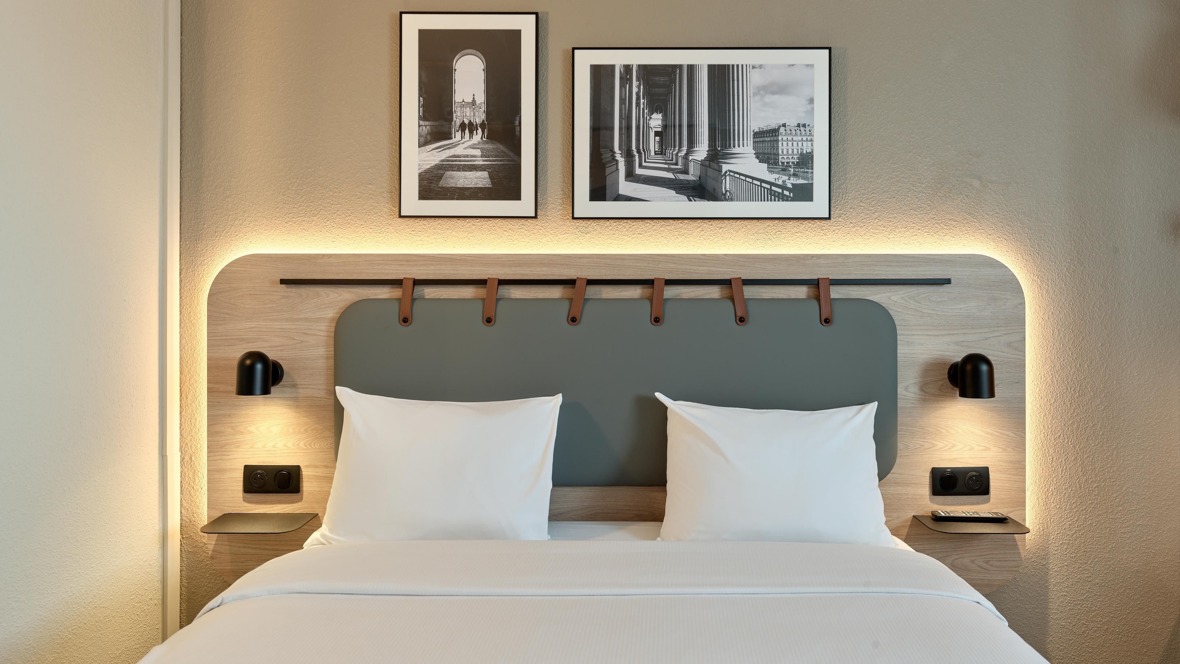 A neatly made bed with a headboard featuring a light fixture and two wall-mounted lamps.