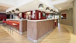 A modern bar area with a wooden counter, red bar stools, and pendant lighting. - Campanile PRIME - Villejuif (Villejuif)