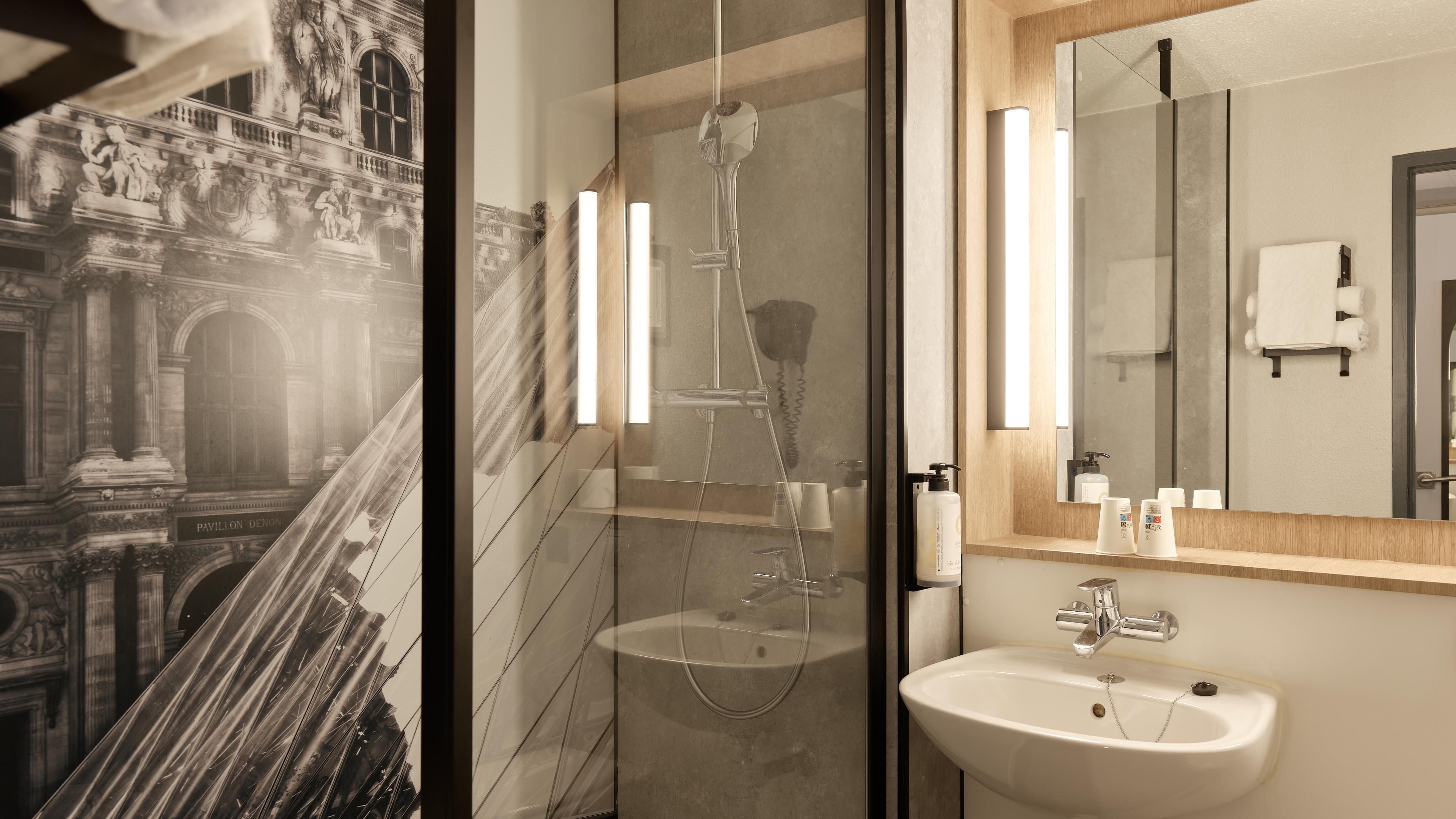 Un baño con un espejo grande, un lavamanos y una ducha.
