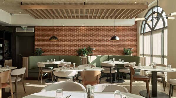 A restaurant interior with brick walls, green seating, and round tables.