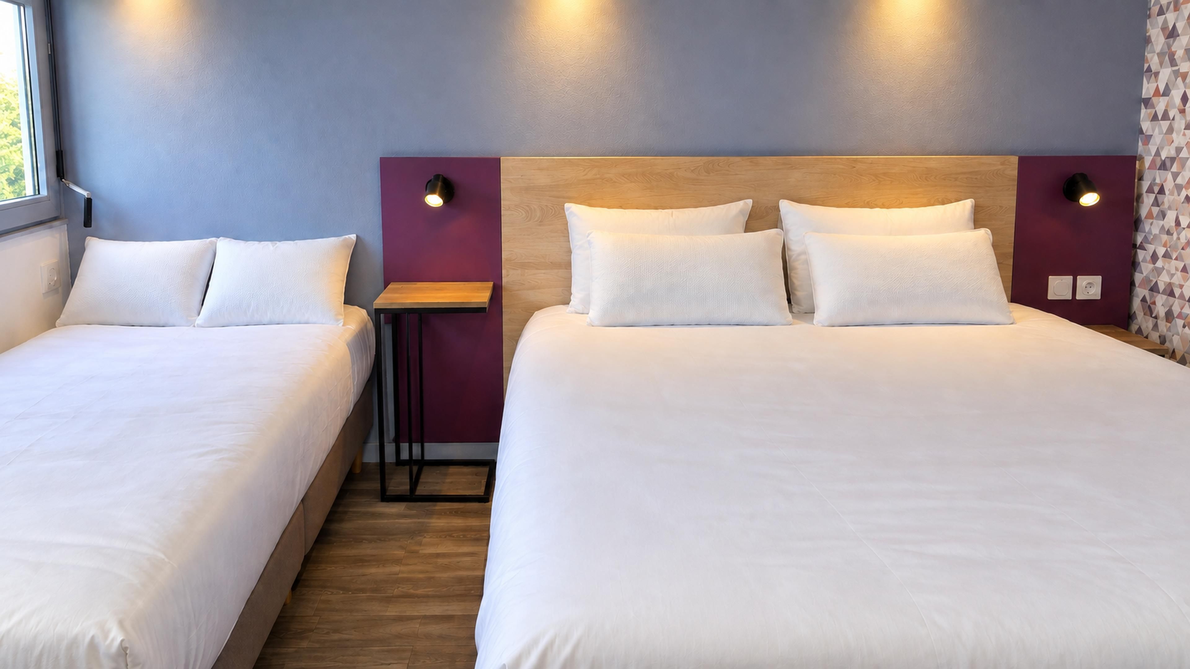 A hotel room with two single beds, a small table, and a nightstand with lamps.