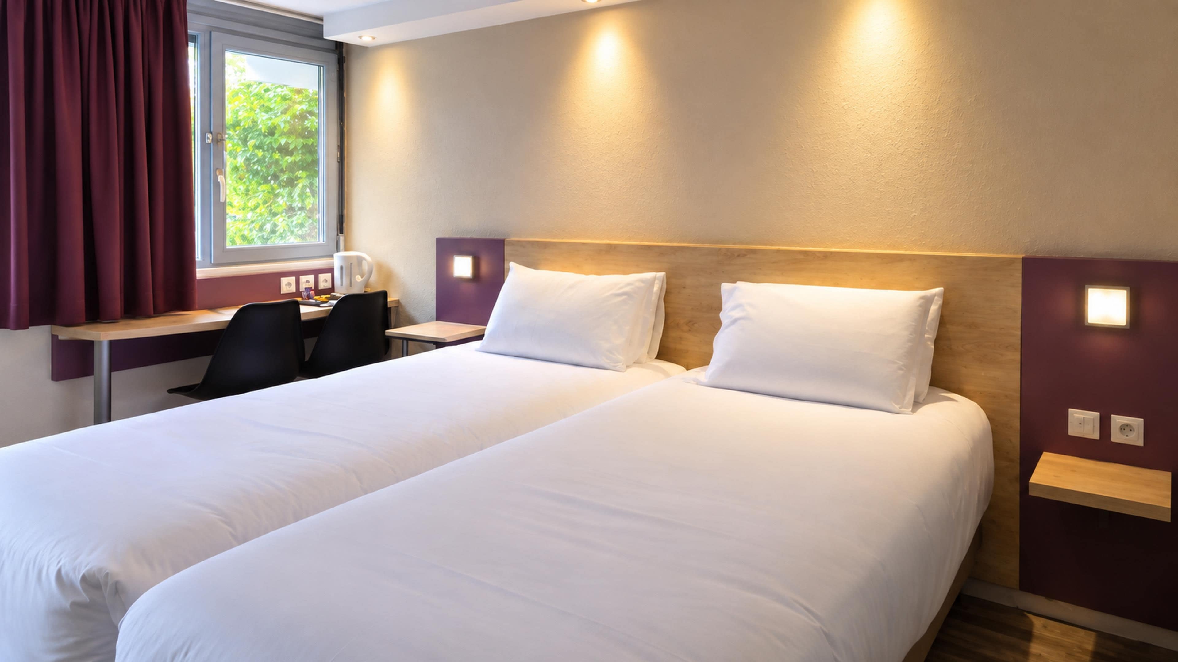 A hotel room with two beds, a desk, and a chair.
