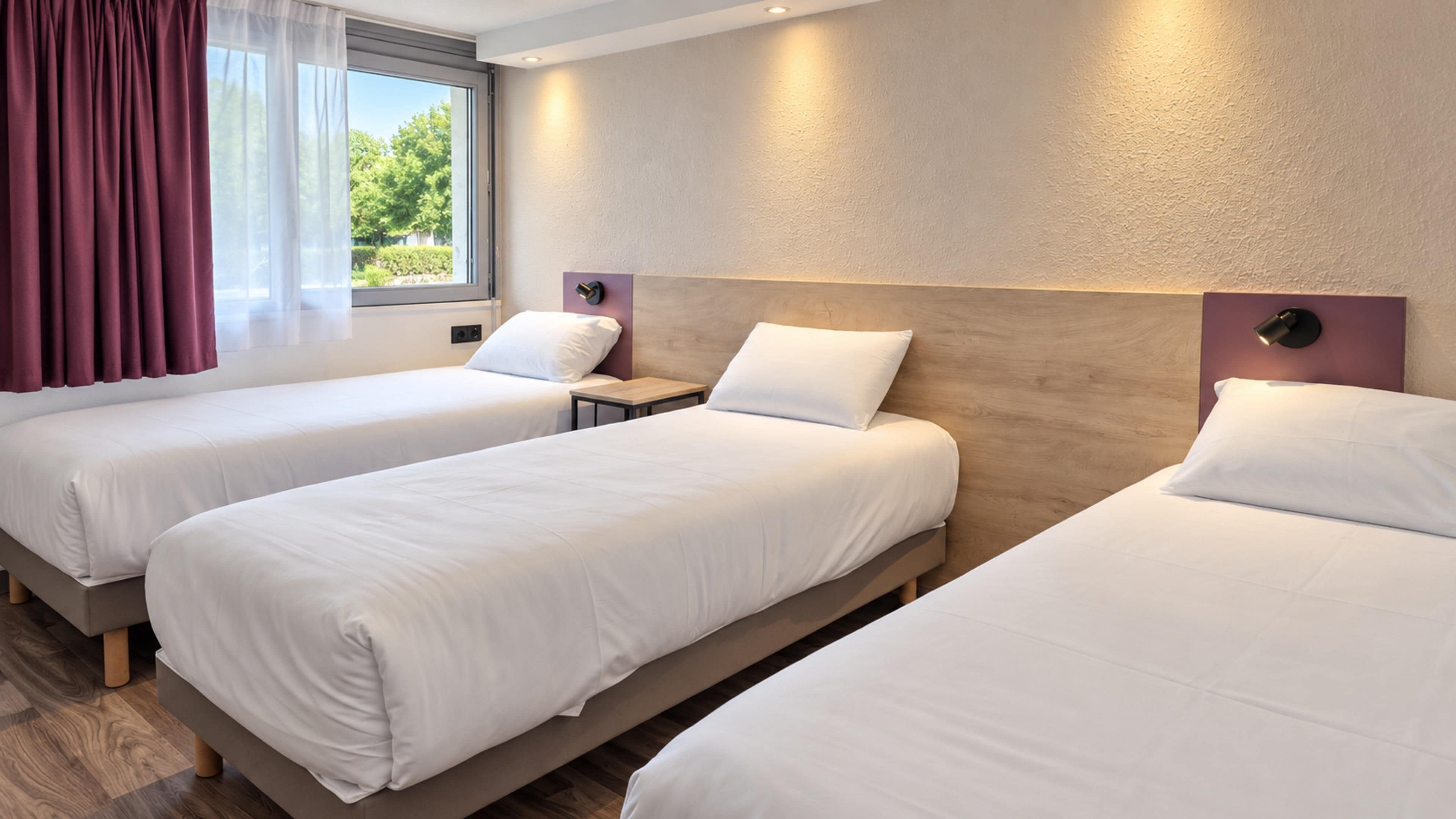 A hotel room with two single beds, a nightstand, a window with curtains, and a wall-mounted lamp.