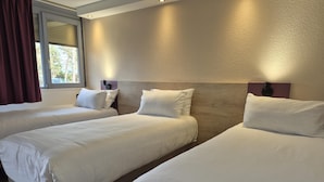 Quarto de hotel com três camas, janela com cortinas e parede texturizada.