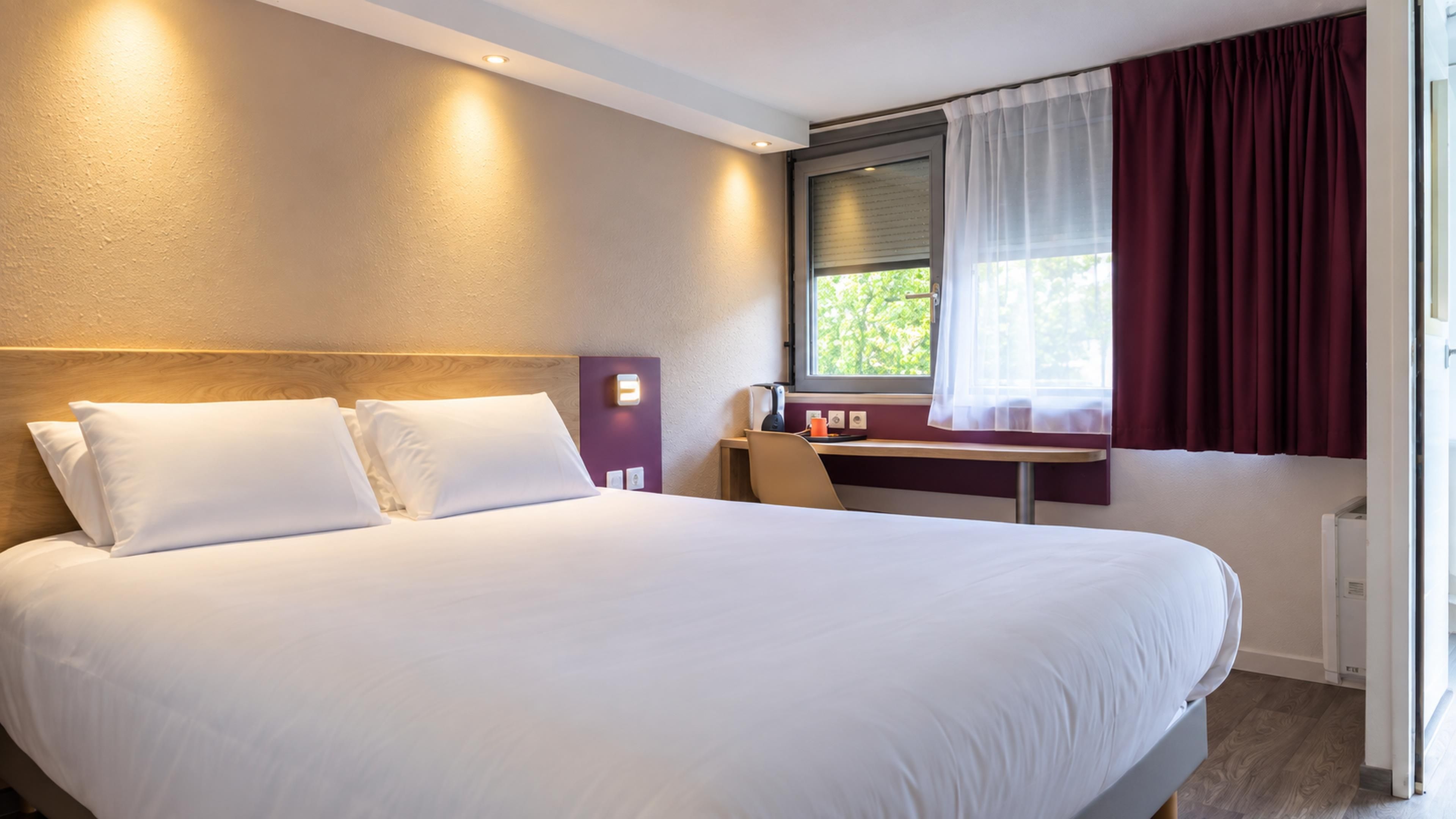Una habitación de hotel con una cama grande, un escritorio y una ventana con cortinas.