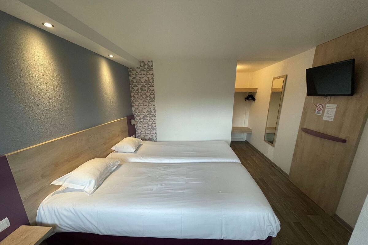 Et hotelværelse med to senge, et træhovedgærde, et tv ophængt på væggen og et spejl.