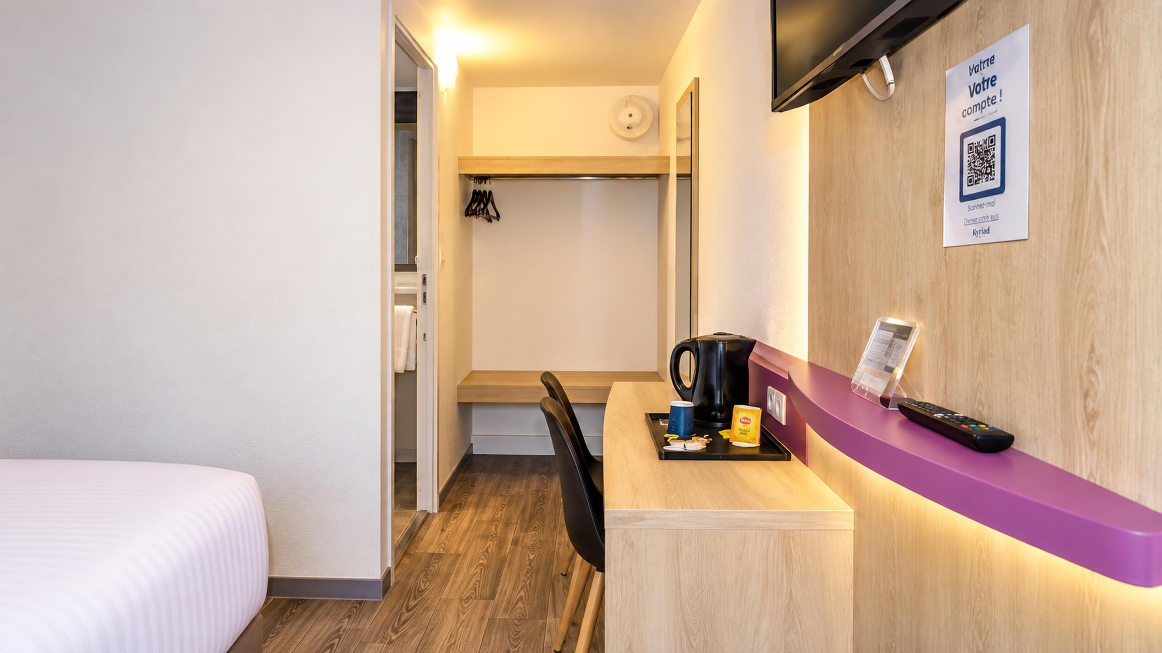 Habitación de hotel con cama, escritorio con cafetera, control remoto y código QR para registro digital.