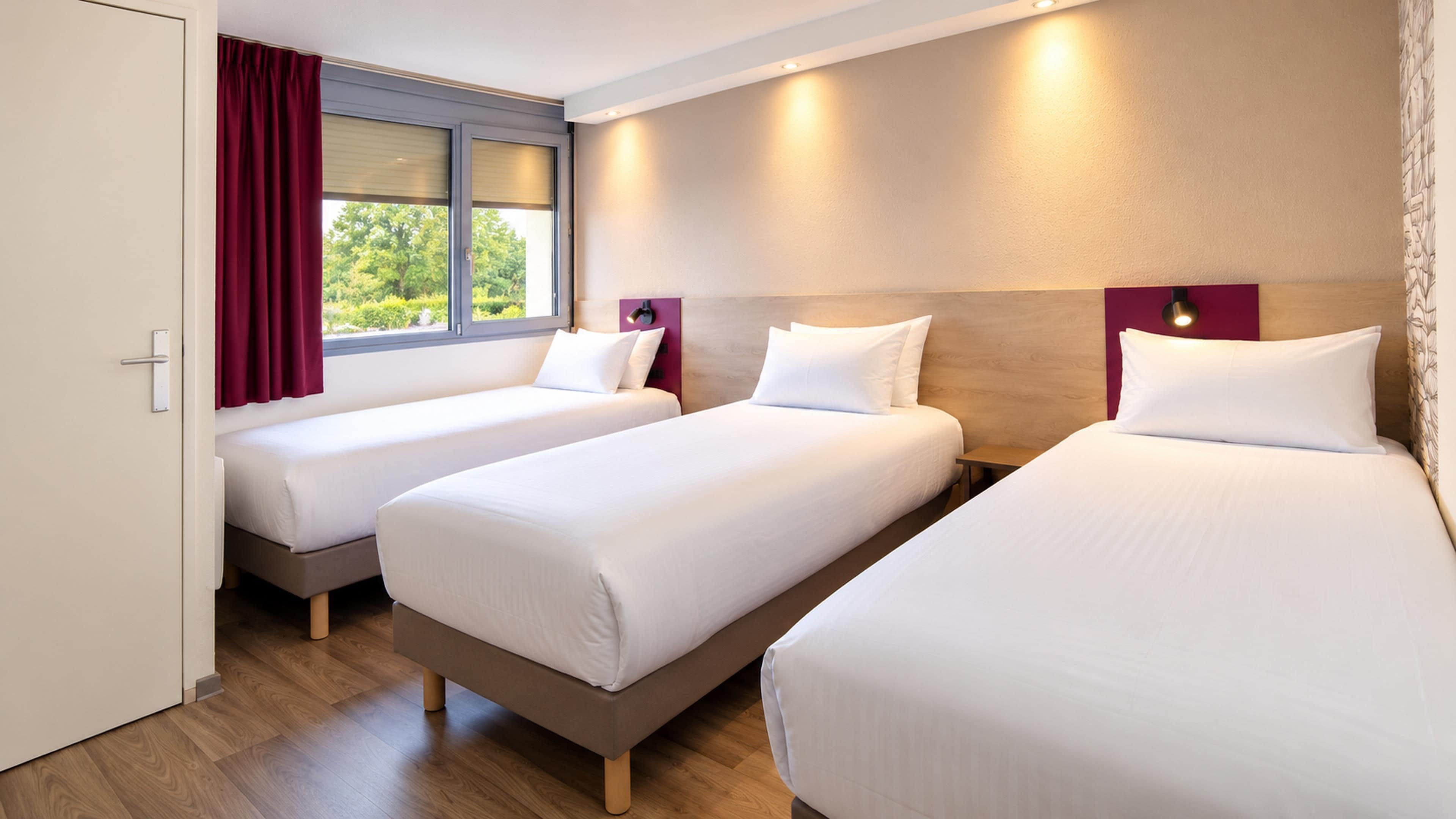 Una habitación de hotel con tres camas individuales, una ventana con cortinas y una puerta.