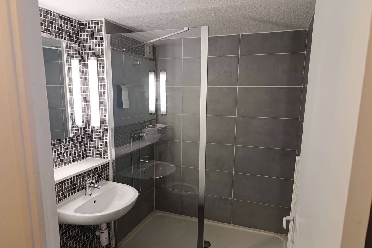 Et badeværelse med en brusekabine i glas, en hvid vask og et flisebeklædt backsplash.