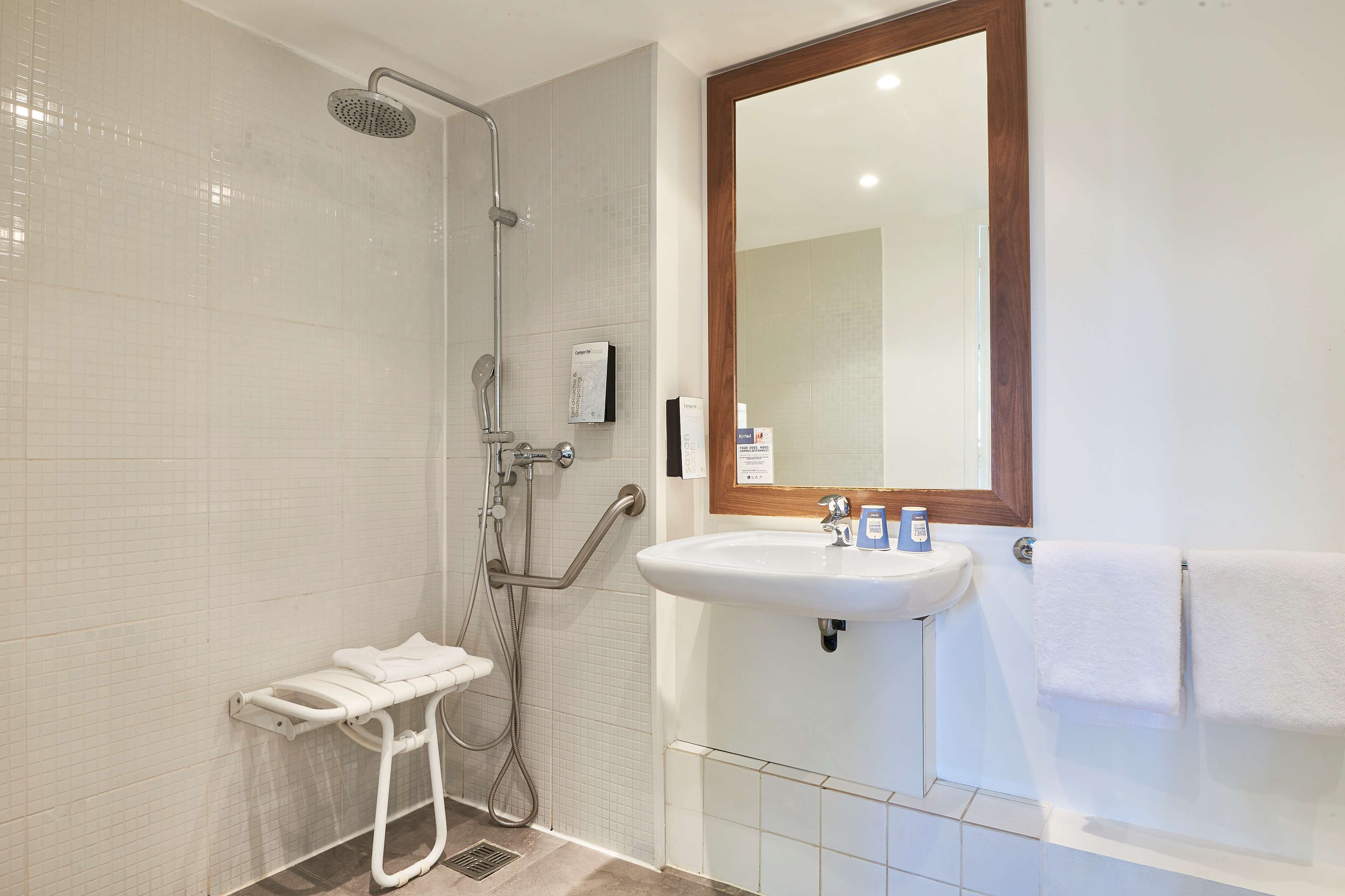 A bathroom with a shower, a sink, a mirror, and a towel rack.